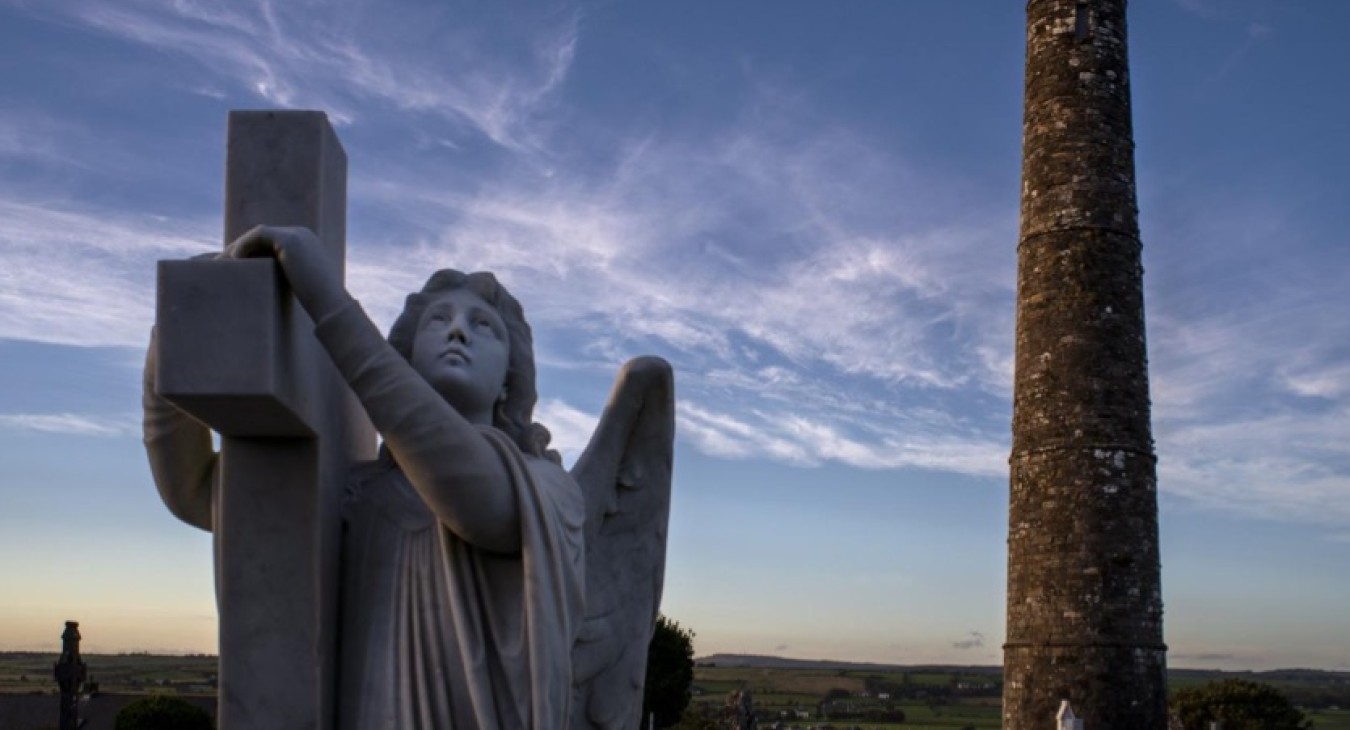 An angel embracing a cross and a pointed round tower in the background