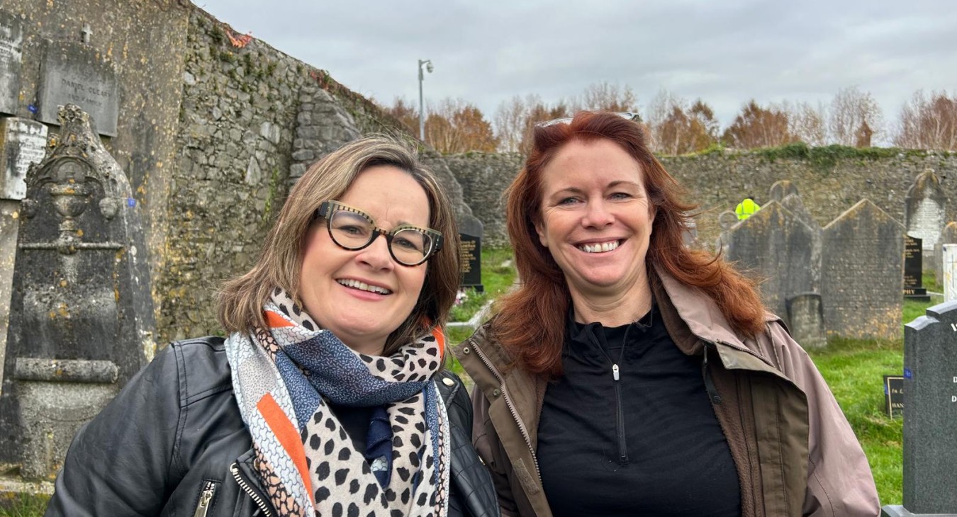 Two project members, Ciara and Ella, in photograph. Gray limestone wall and gravestones in background